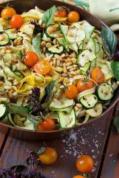 a bowl filled with zucchini, tomatoes and other veggies on top of a wooden table