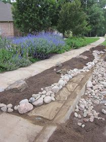 there is a long row of rocks on the side of the road with purple flowers in the background