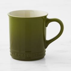 a green coffee mug sitting on top of a white marble countertop with the word le creuset written across it