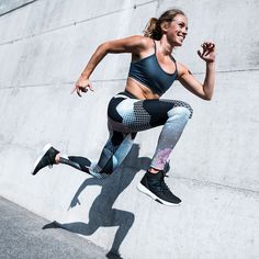 a woman is jumping in the air while wearing leggings and sports bra top