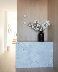 a vase with flowers sitting on top of a marble counter in front of a wooden wall