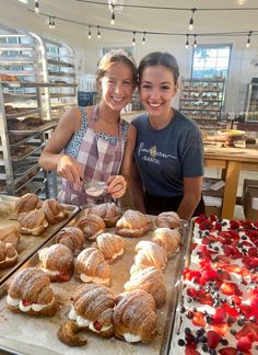 two women standing in front of trays of pastries