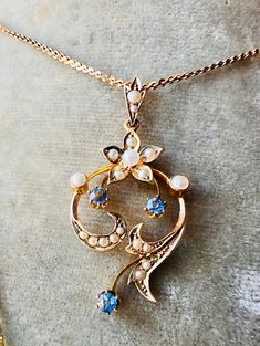 This exquisite pendant showcases a beautiful floral design, set with three faceted sapphires of a stunning cornflower blue shade, along with natural pearls, all encased in 9 carat gold. A stunning representation of the Art Nouveau movement, it emphasizes organic, flowing lines and natural motifs.  The vibrant cornflower blue sapphires and lustrous pearls, set against the warm tones of yellow gold, create a harmonious and elegant piece that captures the essence of the Art Nouveau period. The use Blue Pearl Pendant Fine Jewelry, Fine Blue Pearl Pendant Jewelry, Blue Flower Pendant Jewelry For Wedding, Elegant Blue Flower Pendant Jewelry, Formal Blue Pearl Pendant Jewelry, Formal Blue Jewelry With Pearl Pendant, Natural Motifs, Cornflower Blue, Design Set