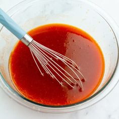 a glass bowl filled with sauce and whisk on top of a white counter