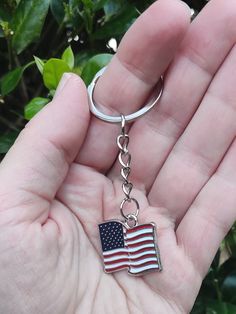 a person is holding an american flag shaped keychain in their left hand,