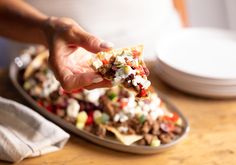 a person holding a piece of food on top of a pan filled with meat and veggies