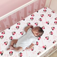 a baby sleeping in a crib with minnie mouse sheets on it's side