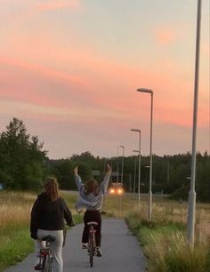 two people riding bikes down a sidewalk at sunset