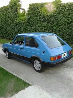 a blue car parked on the side of a road next to a lush green hedge