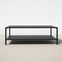 a black coffee table sitting on top of a cement floor next to a white wall