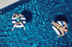 two people floating on inflatable rafts in a swimming pool with blue water