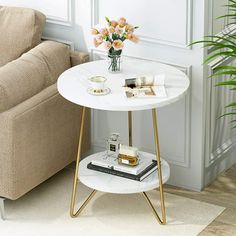 a white table with gold legs and flowers in a vase next to a beige couch