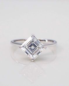 an engagement ring with a princess cut diamond in the center, on a white surface