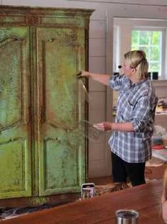 a woman is painting an old green cabinet