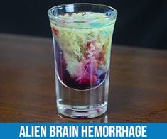 a glass filled with colored liquid sitting on top of a wooden table next to a sign that reads, alien brain hemorphage