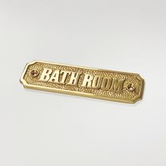 a gold bath room sign on a white surface with the word'bath room'written below it