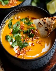 two black bowls filled with soup and garnished with cilantro, parsley and tortilla chips