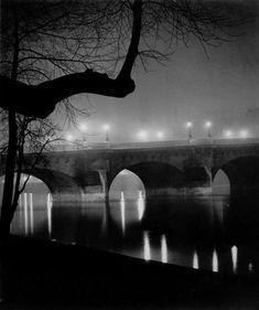 an old photo of a bridge at night with lights reflecting in the water and trees