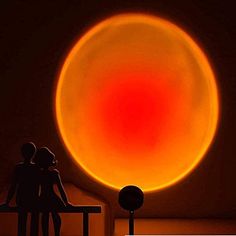 two people are sitting on a bench in front of a large orange object that looks like a sun