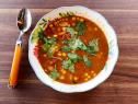 a white bowl filled with soup on top of a wooden table next to a spoon