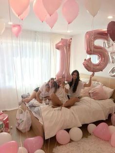 a group of people sitting on top of a bed with balloons in the shape of numbers