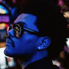 a man with dark hair and sunglasses on his face looking off into the distance in front of neon lights