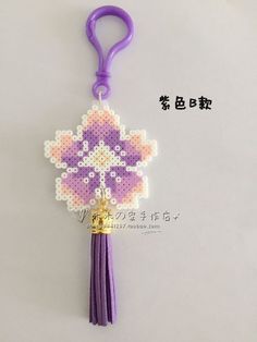 a purple key chain with a cross stitch design on it and a bell hanging from the end