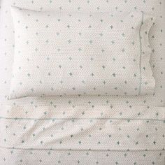 a bed with white sheets and green stars on it's pillowcase, next to a pair of pillows