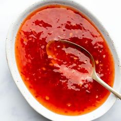 a white bowl filled with red sauce on top of a table next to a spoon