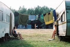 two women sitting on the ground next to an rv and some clothes hanging out to dry