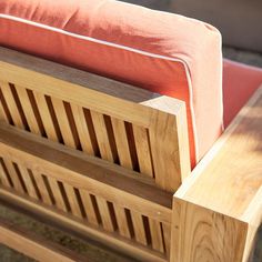 a wooden bench sitting on top of a sidewalk next to a red cushioned pillow