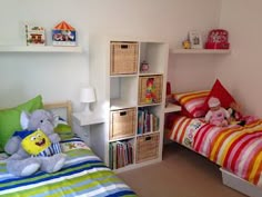 two small children's beds in a bedroom with toys and bookshelves on the wall