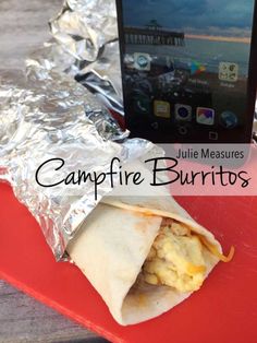 a burrito wrapped in aluminum foil next to a cell phone