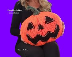 a woman is holding a crocheted pumpkin