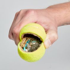 a hand holding a yellow ball filled with small objects in it's opening hole