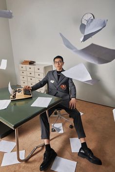 a man sitting at a desk surrounded by papers flying in the air over his head