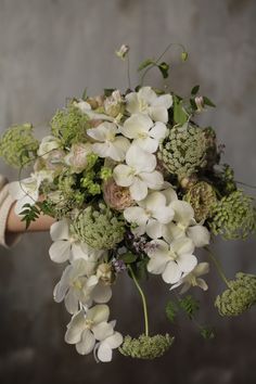 a bouquet of white flowers and greenery is held by a woman's arm