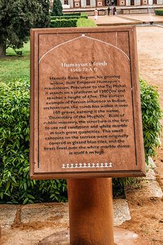 a sign in front of a large building with trees and bushes around it on the side of a dirt road