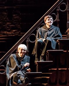 two people sitting on some steps in front of a stair case and another person standing behind them