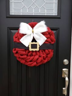 a christmas wreath on the front door is decorated with red and white yarn, black ribbon, and a gold buckle