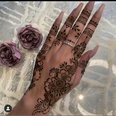 a woman's hand with henna tattoos on it and flowers in the background