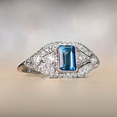 An antique style gemstone and diamond ring that centers a lively emerald cut aquamarine weighing approximately 0.89 carats. The platinum mounting is decorated with old European cut diamonds going east-west. The under-gallery displays stunning open-work.
The approximate measurements of the center gemstone are 6.53mm x 4.32mm.
This ring can be resized to any finger size at no extra cost.
If you have any questions about the Clifden ring, please feel free to contact us. Vintage Blue Sapphire Ring With Diamond Accents, Art Deco Blue Diamond Ring With Center Stone, Blue Art Deco Diamond Ring With Center Stone, Art Deco Topaz Ring With Center Stone, Art Deco Blue Diamond Ring With Rose Cut, Art Deco Blue Diamond Ring With Accents, Blue Art Deco Diamond Ring With Rose Cut, Heirloom Blue Diamond Ring With Accents, Blue Art Deco Diamond Ring With Accents