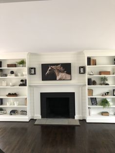 an empty living room with white bookcases and a fire place in the center