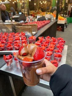 a person holding up a plastic cup with strawberries in it and chocolate on top