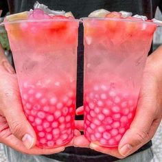 two people holding up drinks in plastic cups with strawberries on the rim and ice