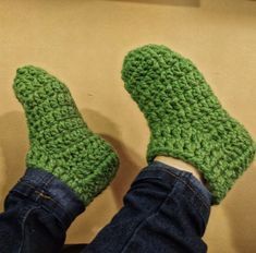 someone is wearing green crocheted slippers with their feet propped up on a couch