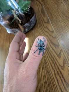 a person's finger with a blue spider tattoo on it, next to a potted plant