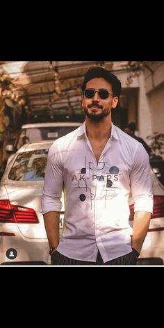 a man standing in front of a car wearing sunglasses and a white shirt with black writing on it