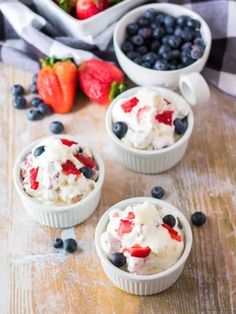 three small bowls filled with fruit on top of a wooden table next to strawberries and blueberries