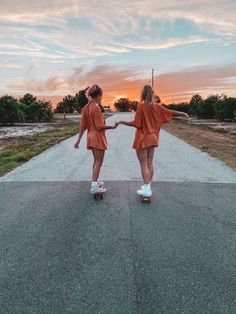 two girls in orange dresses skateboarding down a road at sunset or dawn with the sun setting behind them